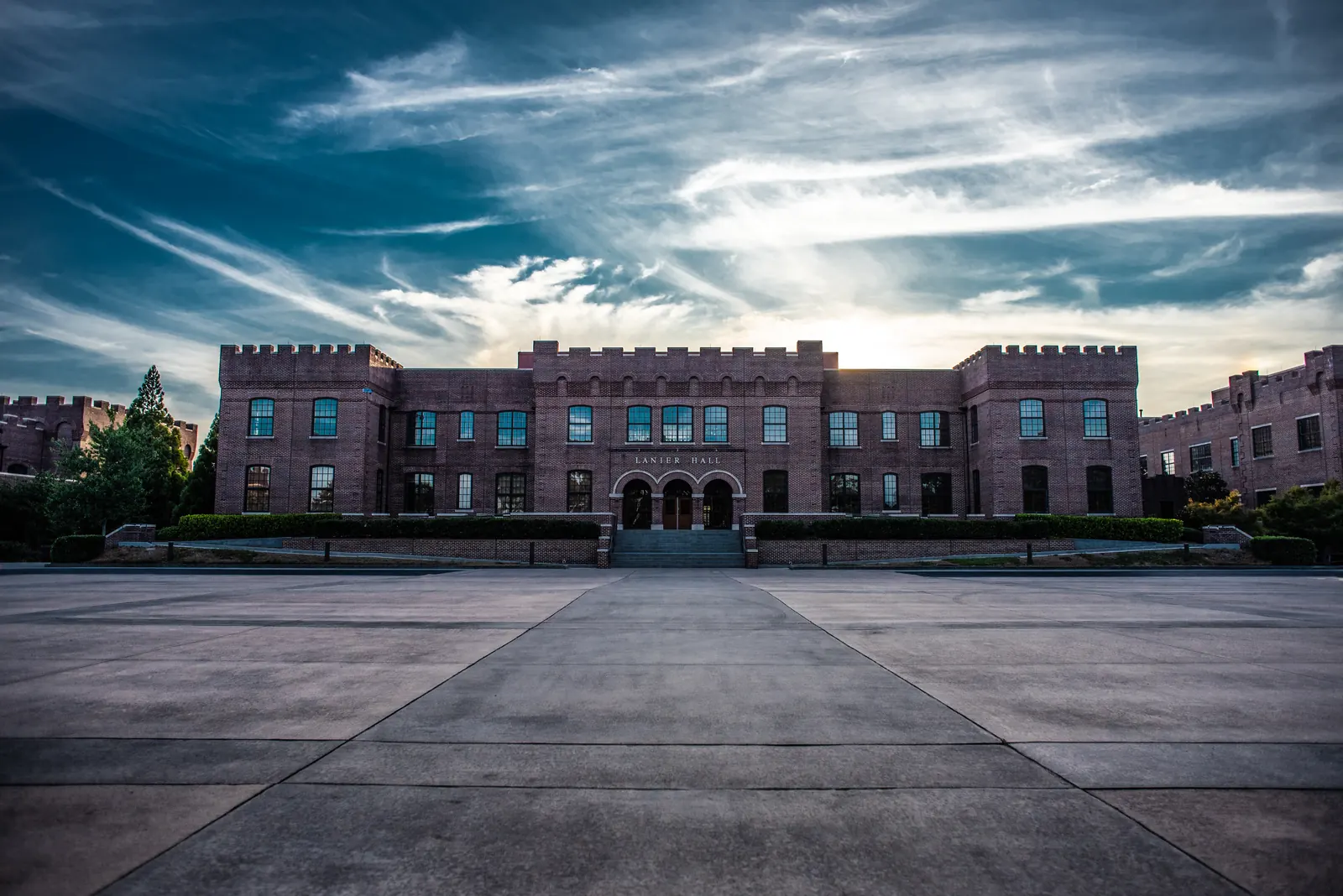 A crenellated red-brick castle-style building with 'LANIER HALL' over its arched entrances faces a wide concrete plaza under a dramatic streaked sky.
